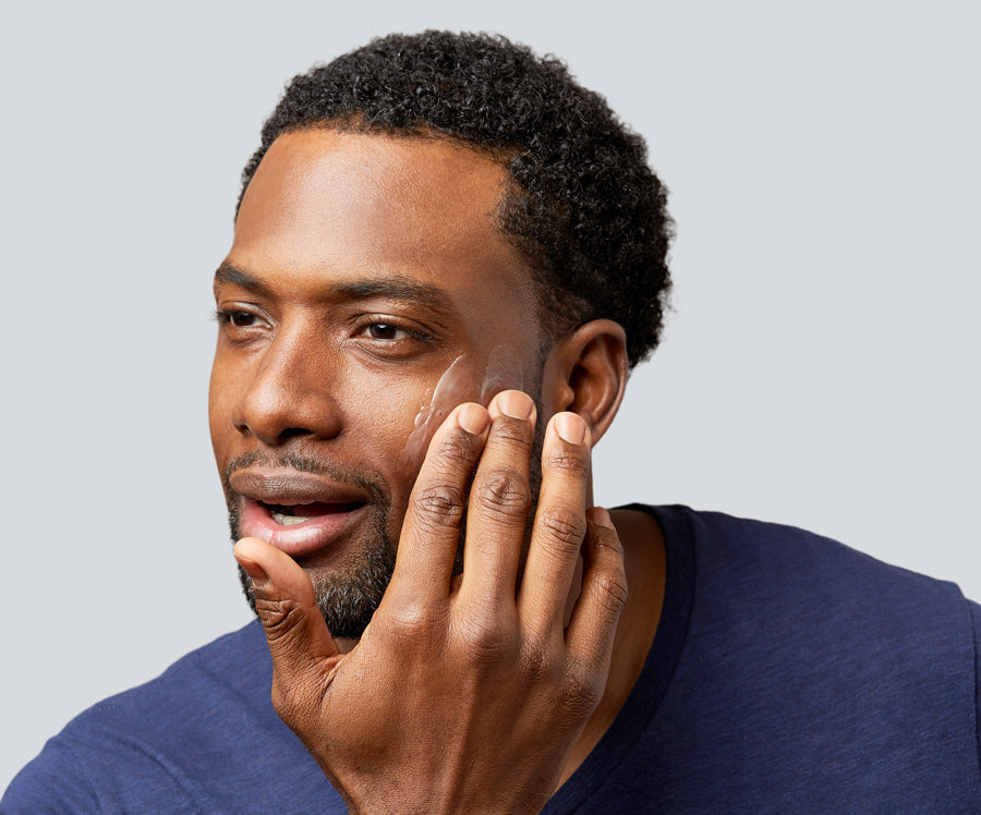 Man applying facial moisturizer to his right cheek with fingertips.