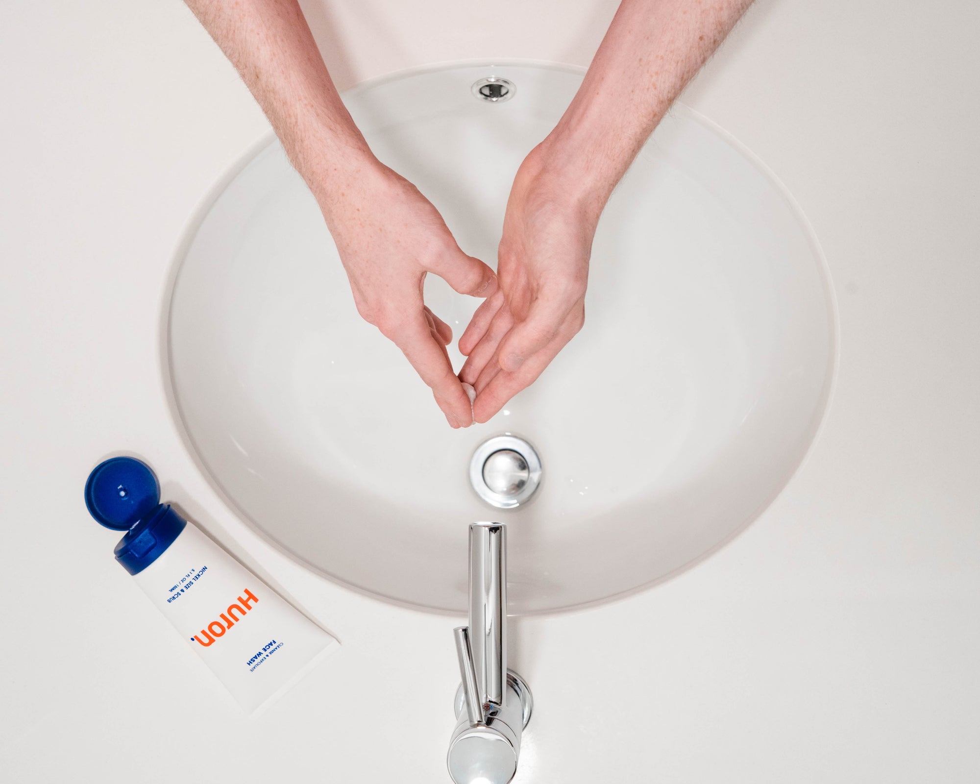 Person washing hands at a sink with Huron grooming product nearby