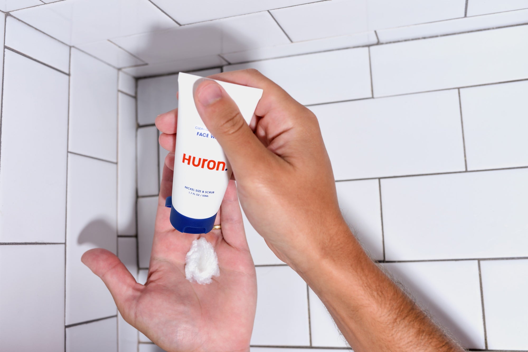 Hand squeezing foam from Huron. tube into palm; tube text: FACE WASH, Huron., NICKEL SIZE & SCRUB, 1.7 FL OZ / 50ML