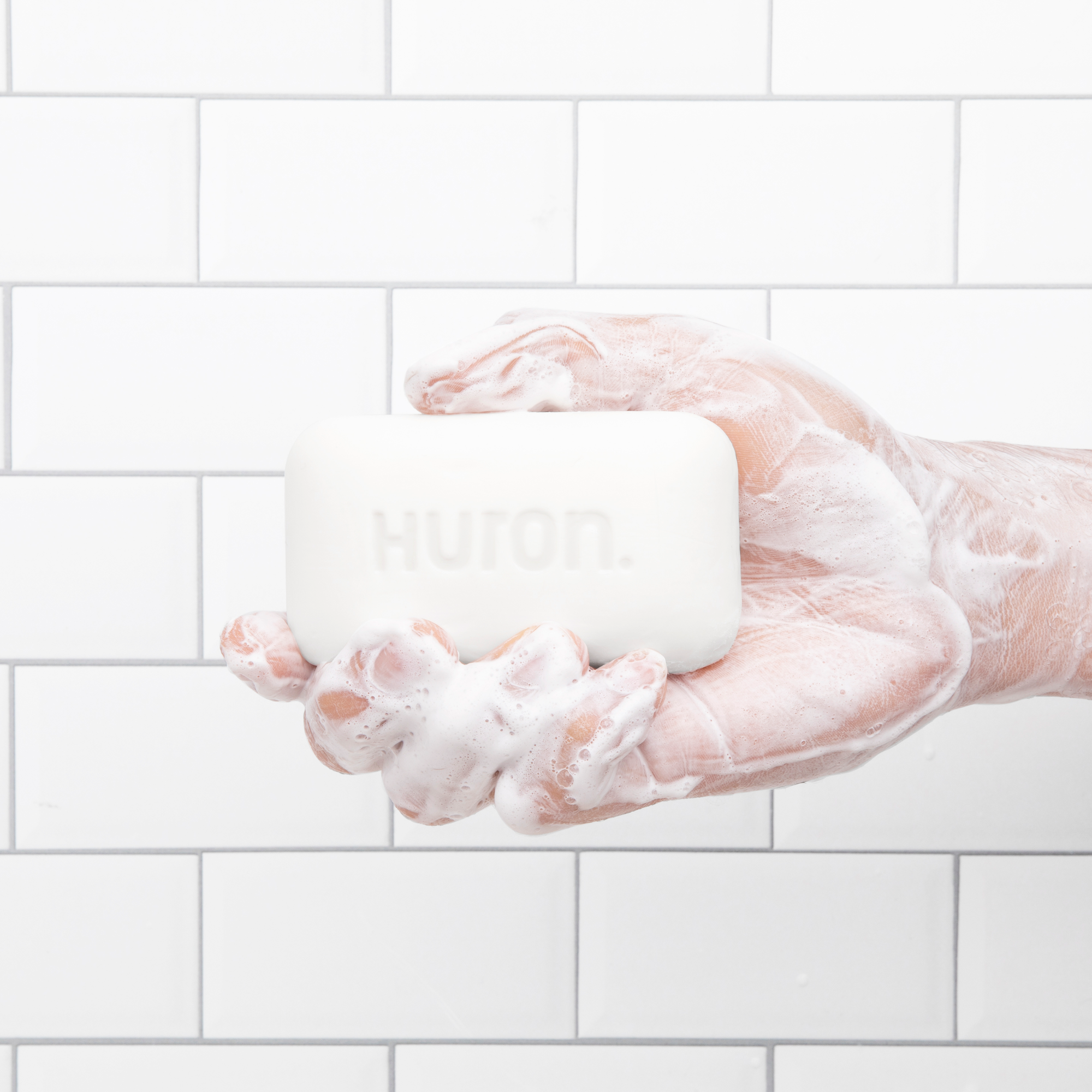 Hand covered in soap suds holding white soap bar embossed HURON.