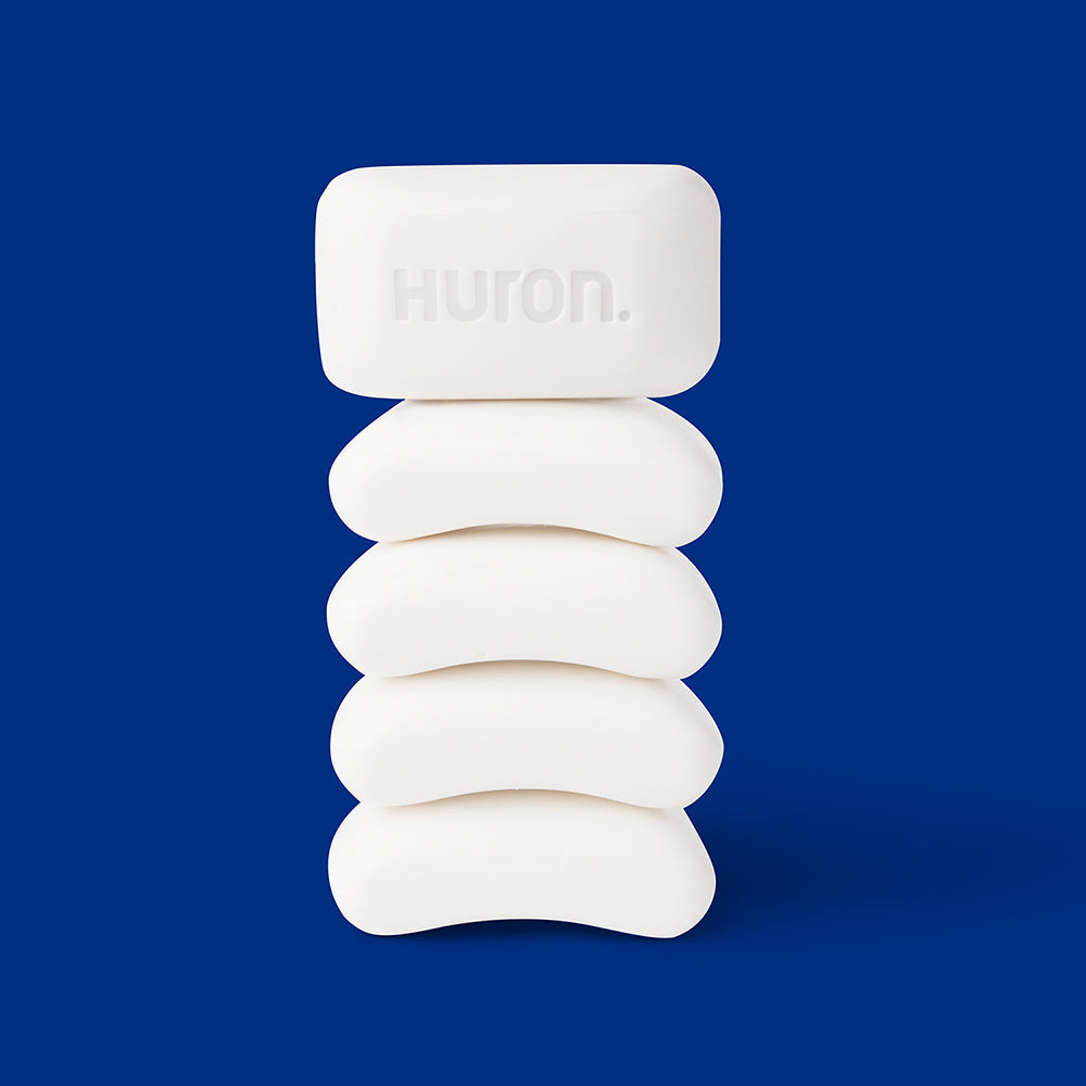 Stack of five white soap bars with Huron. embossed on the top bar against a solid blue background