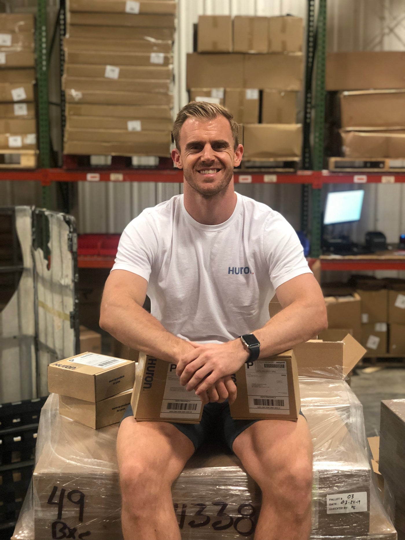 A smiling man sitting on boxes in a warehouse, promoting personal care services.