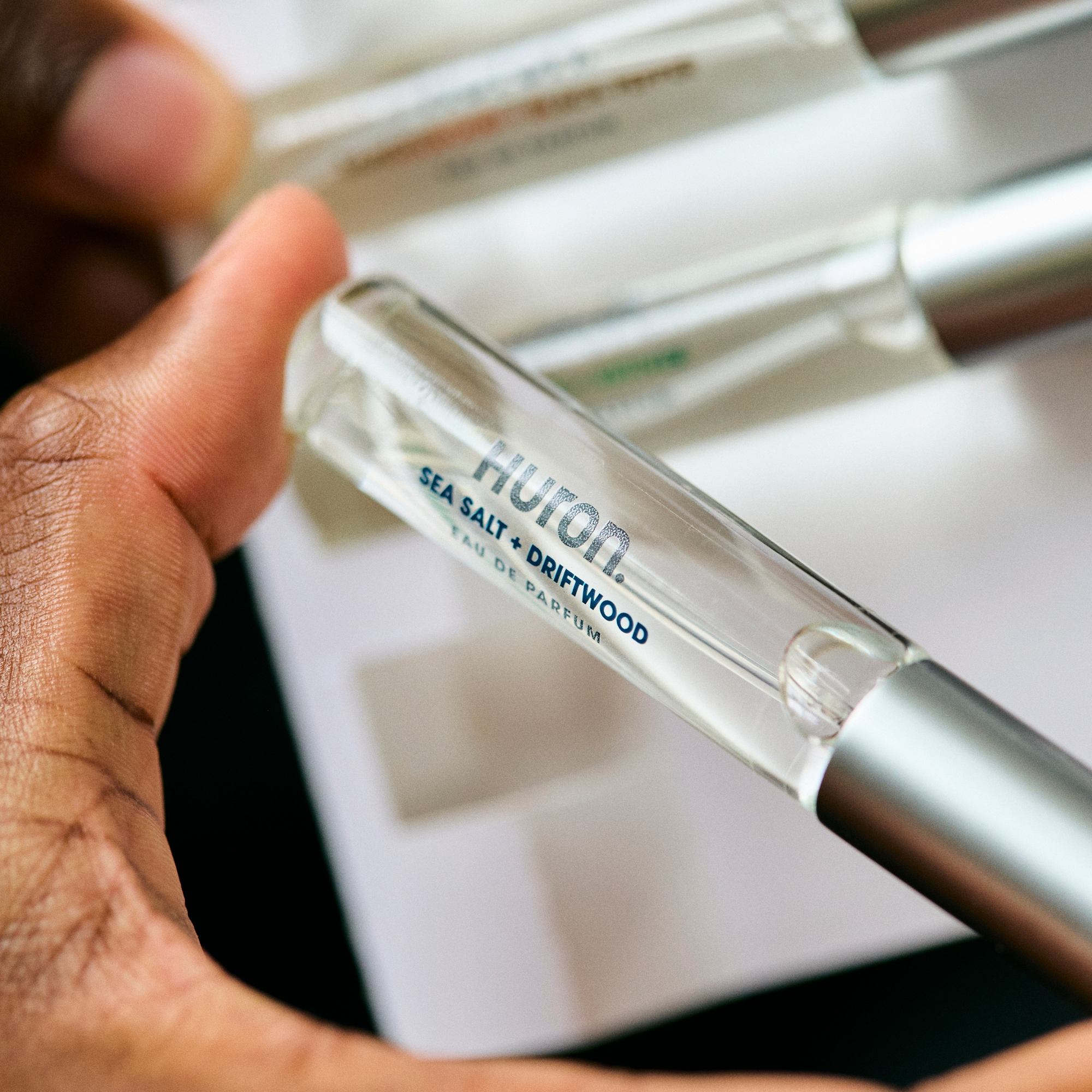 Hand holding a Huron perfume vial labeled 'SEA SALT + DRIFTWOOD EAU DE PARFUM'