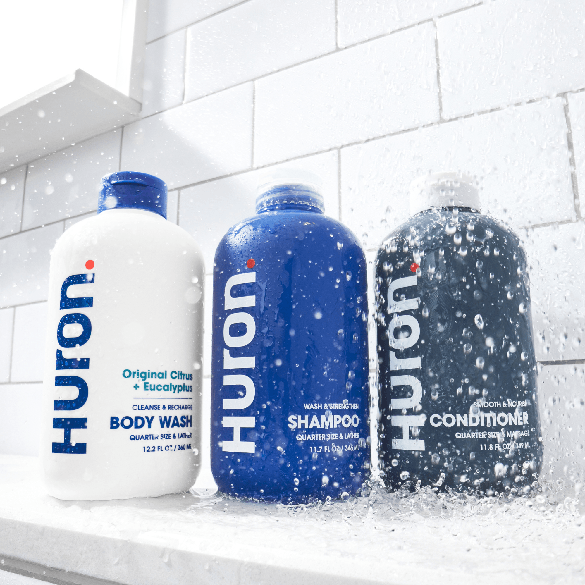 Three Huroni shower bottles: Body Wash (Original Citrus + Eucalyptus), Shampoo (Wash & Strengthen) and Conditioner (Smooth & Nourish) in running shower.