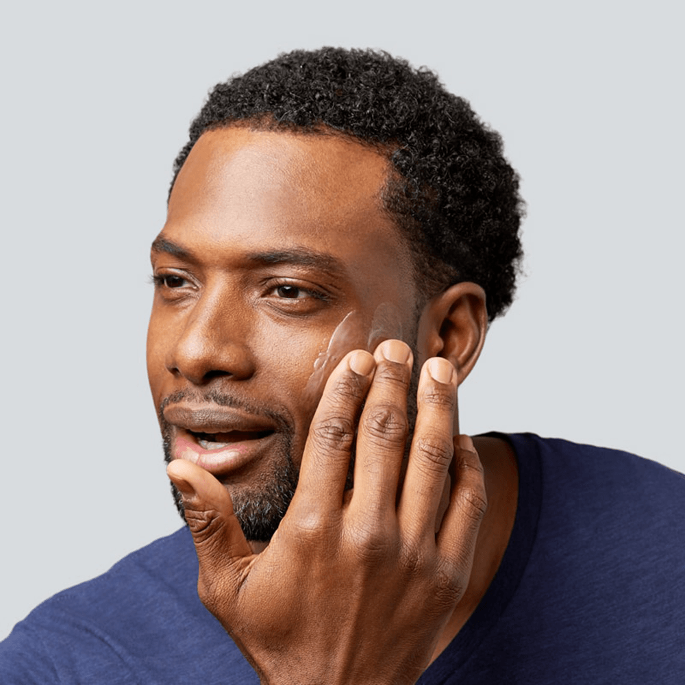 Man applying moisturizer to his cheek, demonstrating skincare routine.