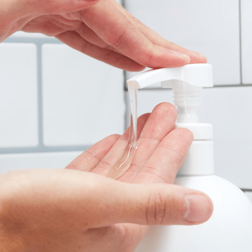Hand pressing a white soap dispenser pump dispensing clear gel soap onto another hand