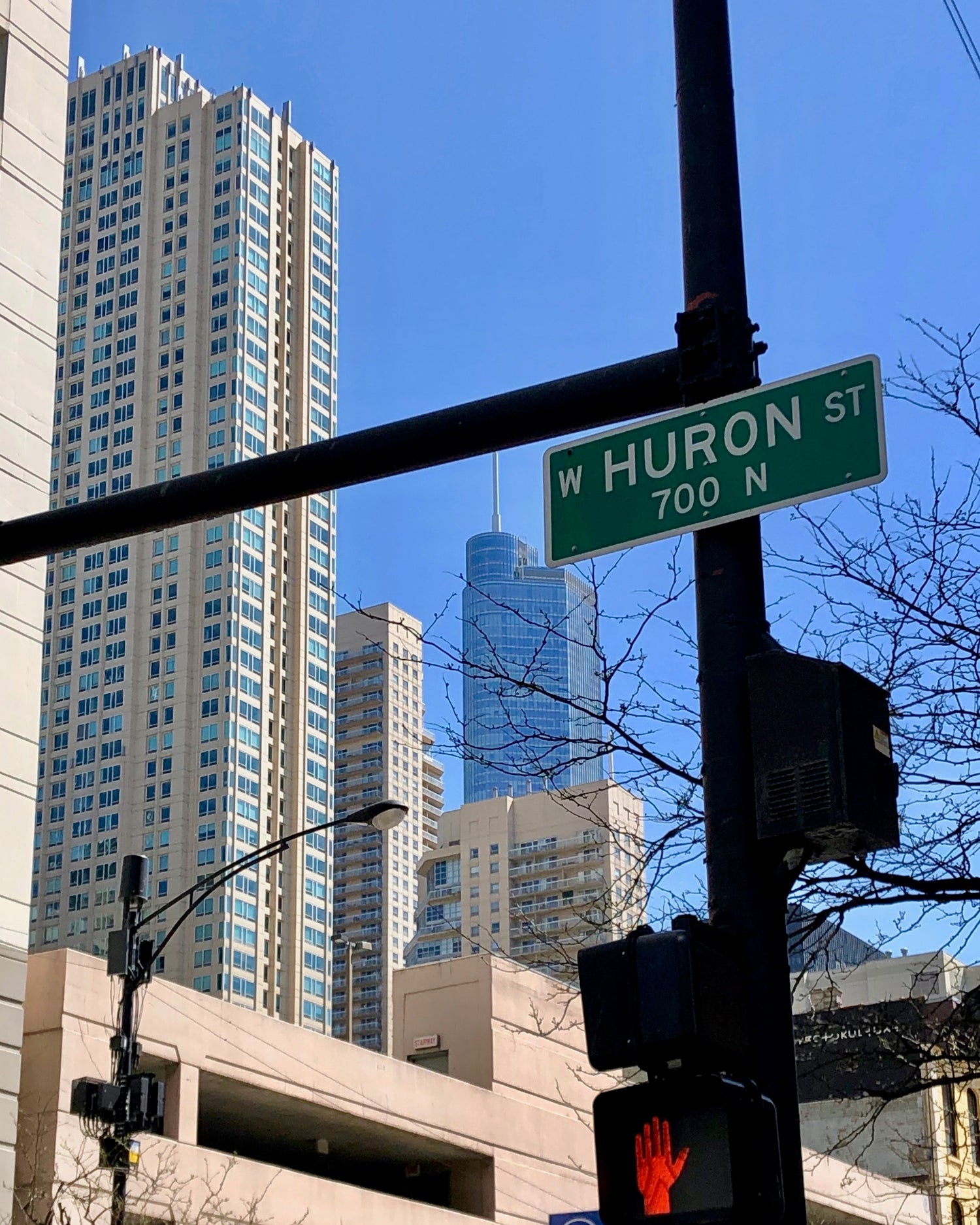 Street sign reading 'W HURON ST 700 N' mounted on a pole with city buildings and a clear blue sky in the background.