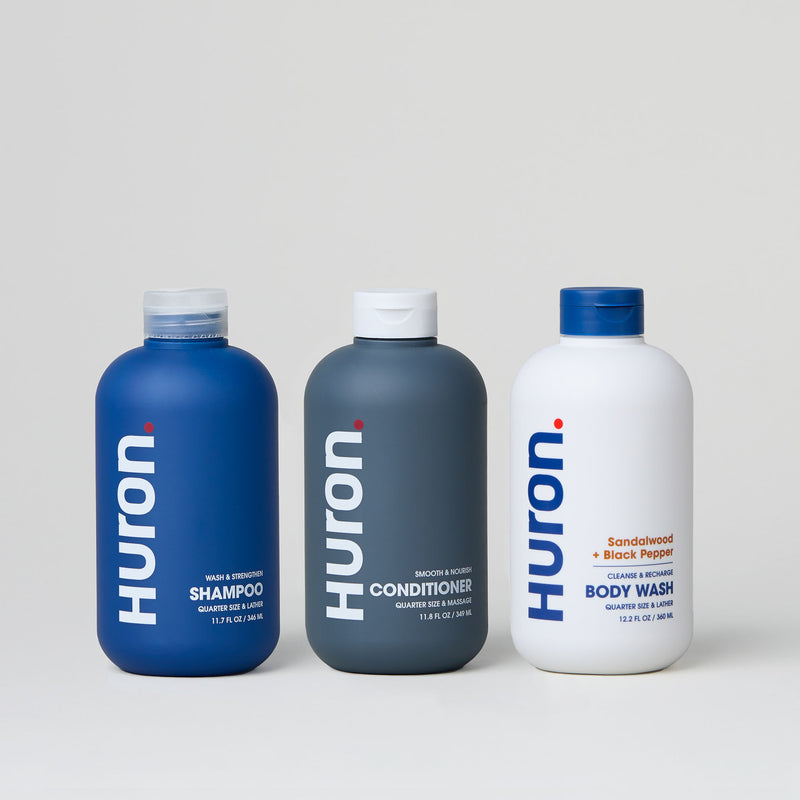 Three Huron personal care products: shampoo, conditioner, and body wash with sandalwood scent.#scent_sandalwood + black pepper