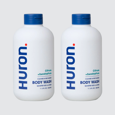 Front view of two Huron Citrus + Eucalyptus body wash bottles (11.3 fl oz) with blue caps on light gray background #scent_citrus + eucalyptus