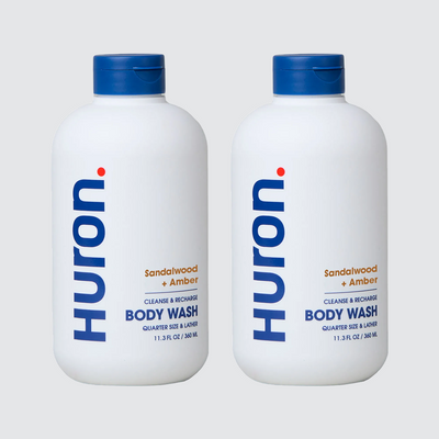 Front view of two Huron body wash bottles (11.3 fl oz) labeled Sandalwood and Amber with vertical Huron logo on light gray background #scent_sandalwood + amber