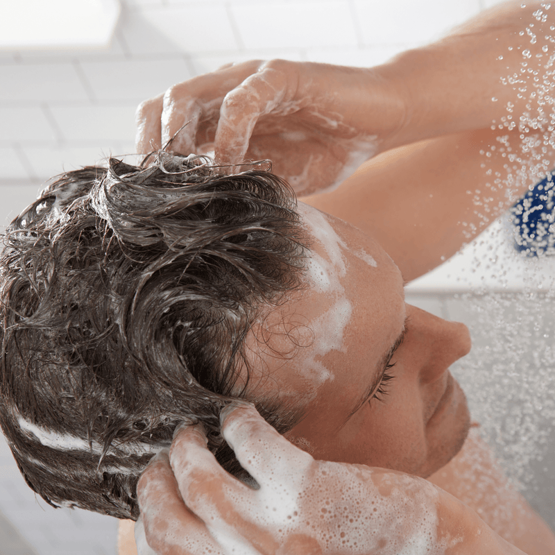Person applying shampoo in the shower with lathered hair