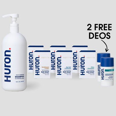 Front view of Huron shower set: jumbo pump shampoo, six soap boxes, and two free deodorants with '2 FREE DEOS' text on gray background #scent_citrus + eucalyptus