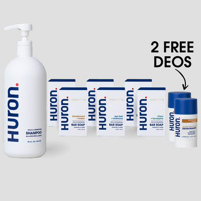Front view of Huron shower set with jumbo shampoo, six bar soaps, and two deodorants; image text: 2 FREE DEOS #scent_sandalwood + amber