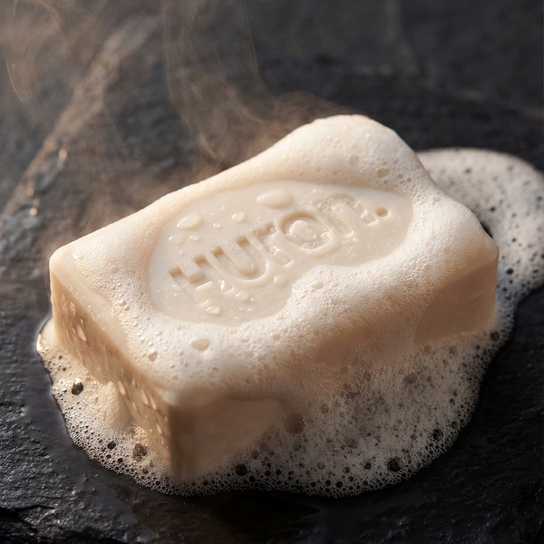 Angled close-up of Huron bar soap showing embossed HURON stamp and rich foamy lather on a dark slate surface