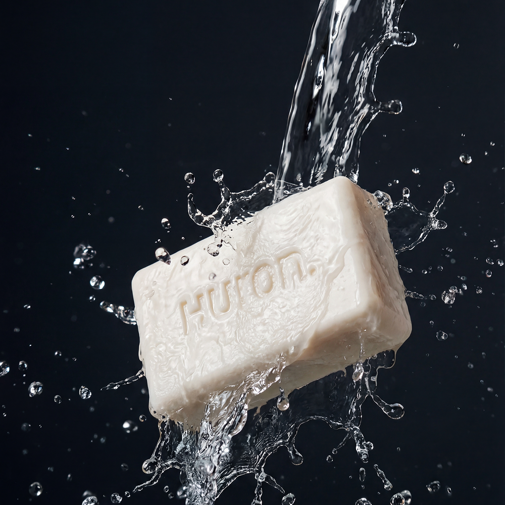 Bar of soap embossed 'Huron.' with water pouring and splash against a dark background.