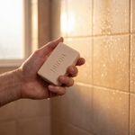 Hand holding a bar of soap with 'Huron' branding in a bathroom setting.