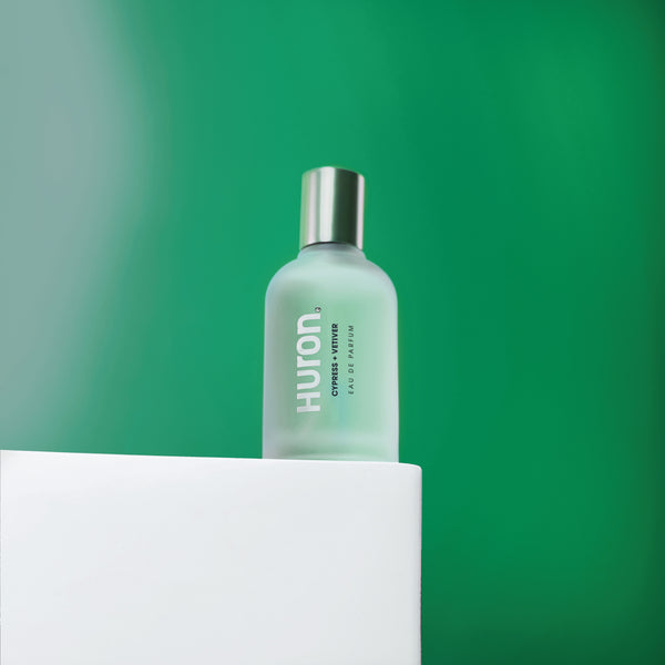 Huron Cypress + Vetiver Eau de Parfum bottle with frosted glass and silver cap on white surface against green background #scent_cypress + vetiver