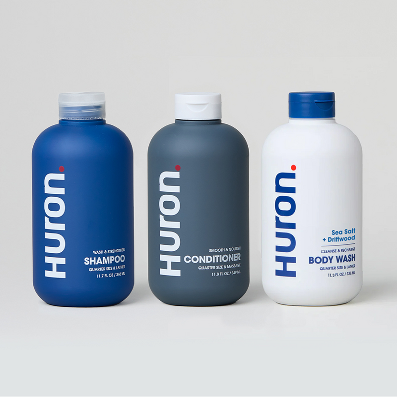 Three Huron personal care products: shampoo, conditioner, and body wash in blue and white bottles.#scent_sea salt + driftwood