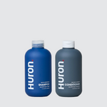 Front view of Huron Hair Duo shampoo (blue, 11.4 fl oz) and conditioner (gray, 11.8 fl oz) bottles on light gray background
