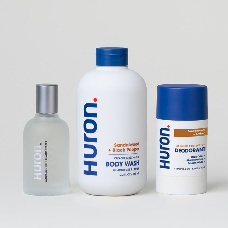 Three Huron products on gray background: Sandalwood + Black Pepper body wash and cologne, and Sandalwood + Amber deodorant. #scent_sandalwood + amber