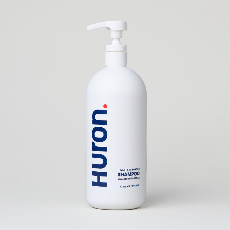 White bottle of Huron shampoo with a pump, labeled 'SHAMPOO' in blue text.