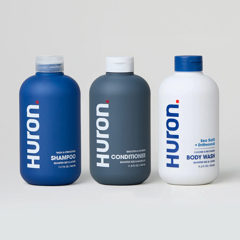 Three Huron personal care products: shampoo, conditioner, and body wash in blue and white bottles.#scent_sea salt + driftwood