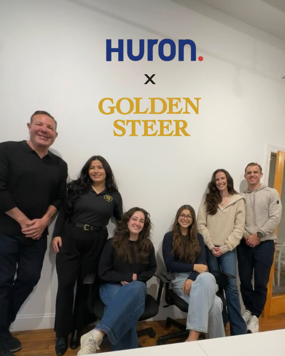 Six colleagues posing under wall signage reading Huron. x GOLDEN STEER