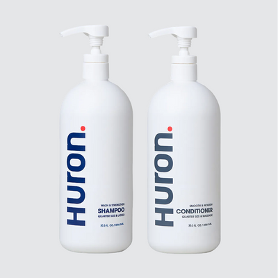 Front view of two jumbo Huron pump bottles: Shampoo and Conditioner showing vertical Huron logo and 30.3 fl oz size on light gray background