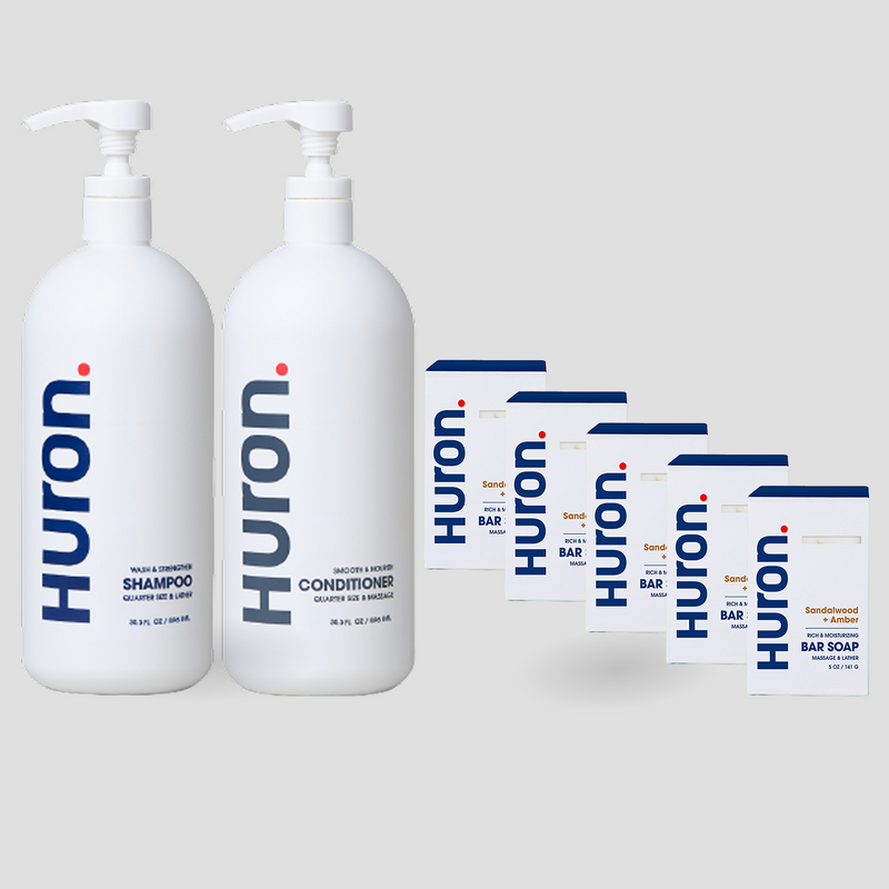 Two white Huron pump bottles labeled Shampoo, Conditioner, and 5 white cartons labeled Huron Bar Soap — Sandalwood + Amber scent. #scent_sandalwood + amber