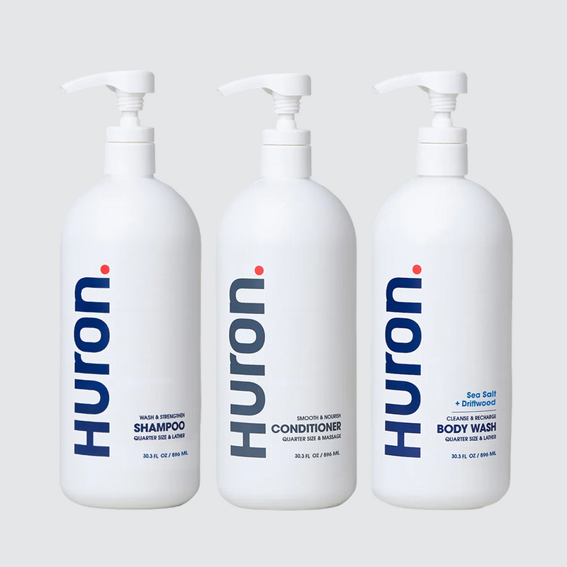 Three white Huron pump bottles labeled Shampoo, Conditioner, Body Wash — Sea Salt + Driftwood scent. #scent_sea salt + driftwood