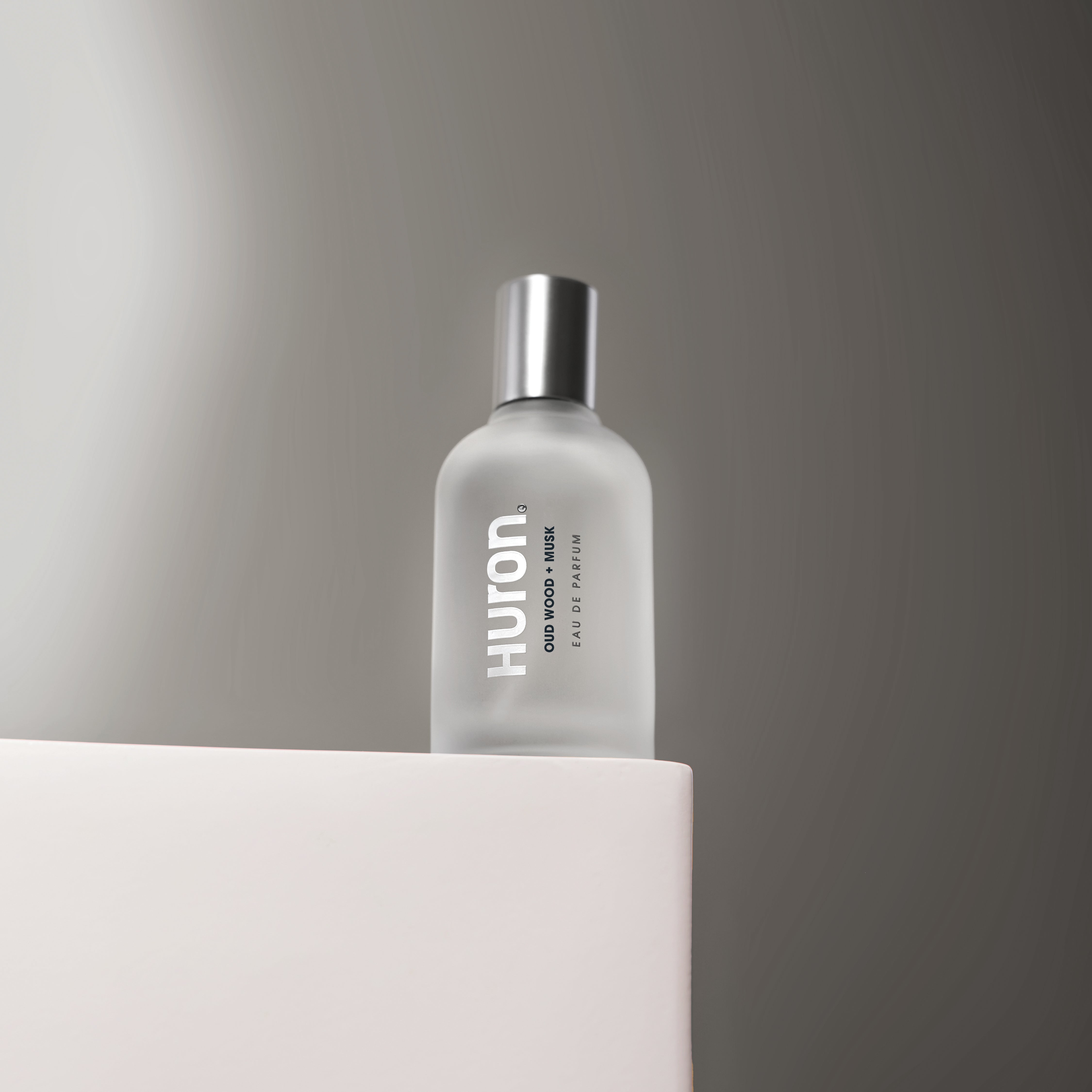 Huron Eau de Parfum bottle with frosted glass and silver cap on pedestal #scent_oud wood + musk