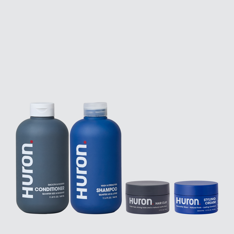 Front view of Huron shampoo, conditioner, hair clay, and styling cream showing product labels on a light gray background