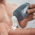 Close-up of Huron conditioner bottle pouring creamy white conditioner into a hand in a tiled shower