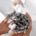 Back view of person washing curly hair, hands massaging thick shampoo lather in a tiled shower.