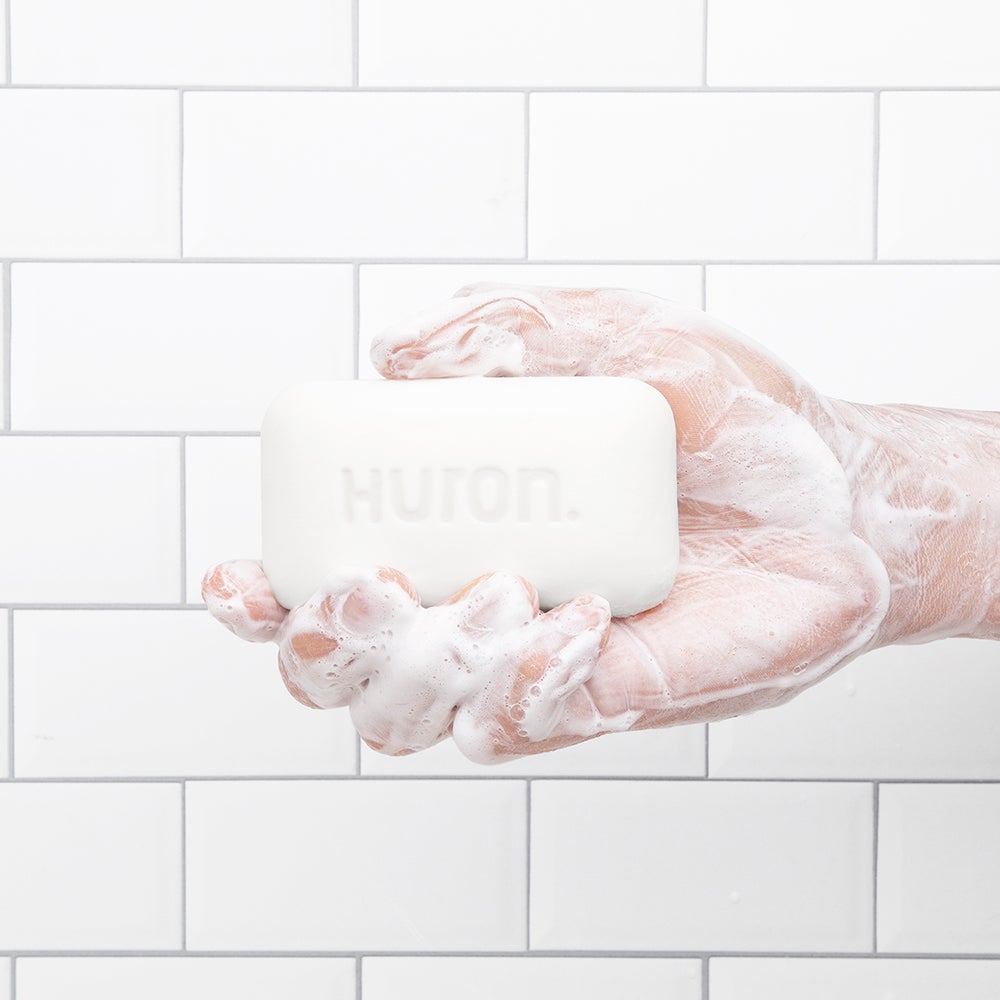 A hand holding a bar of soap with the text 'HURON.' on it, covered in lather.